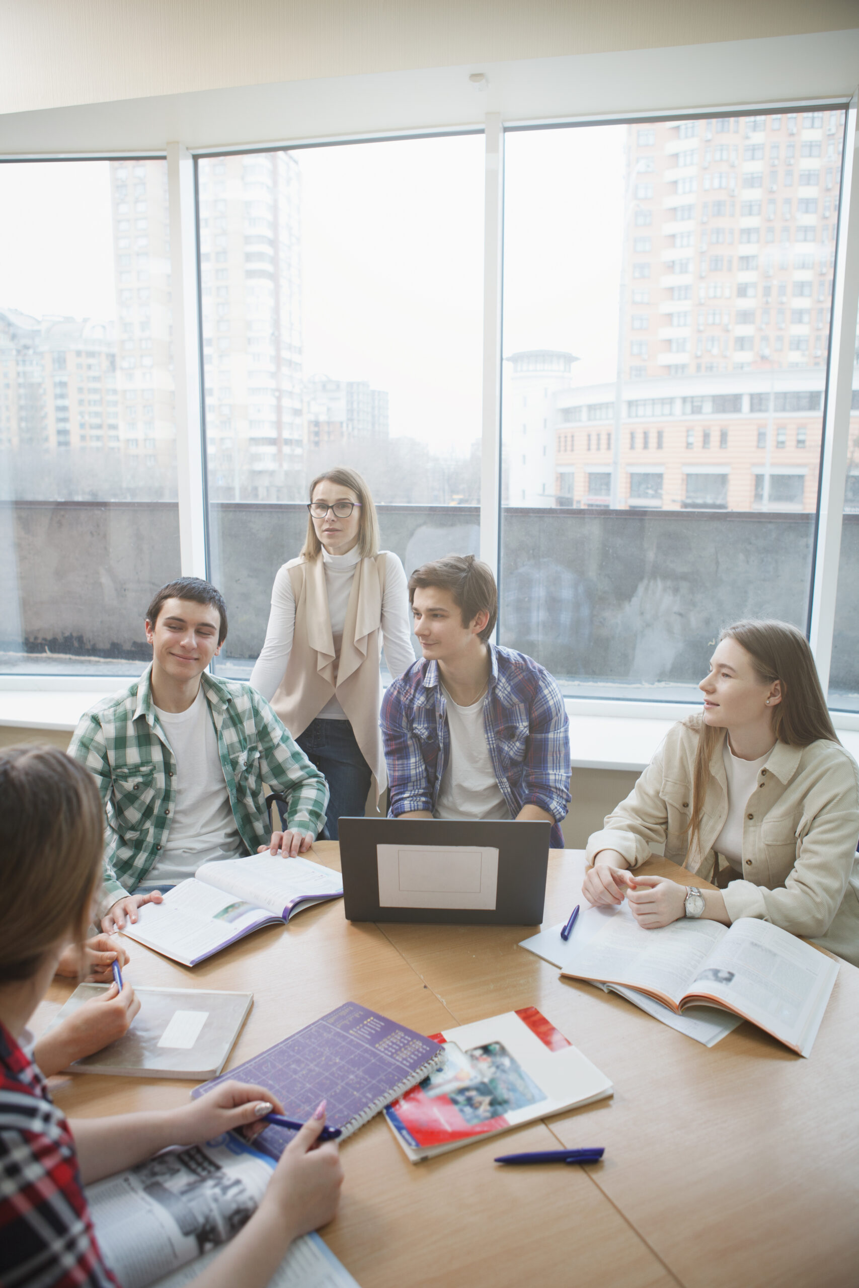 A group of students sitting around a table covered with notebooks, papers and a laptop.