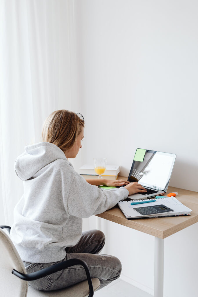 An adukt woman sat at a desk with her back to us. She appears to be studying on a computer.